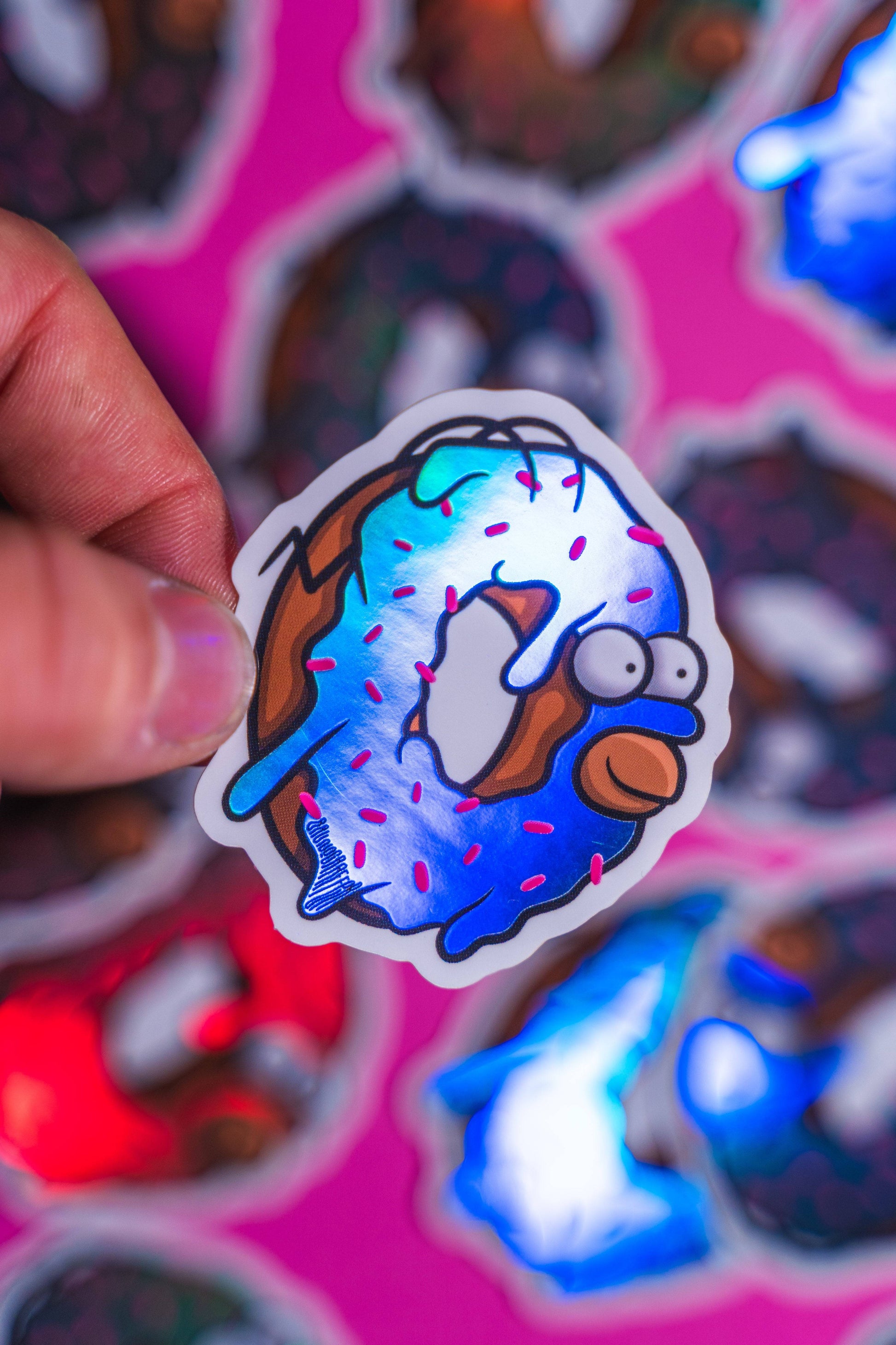 Homer Simpson donut -Illustration digitale imprimée sur stickers Vinyl mat avec effet holographique. Les autocollants sont résistant aux poussières et aux éclaboussures. Veillez bien à les coller sur une surface lisse, propre et sèche pour un bon maintient. Par exemple sur un casque, un vélo, un frigo, une porte, le dos d'un téléphone, etc. Matériaux : Sticker Vinyle mat avec effet holographique.Dimensions : 4,8 x 5,5 cm Vendu à l'unité-Brunograffer